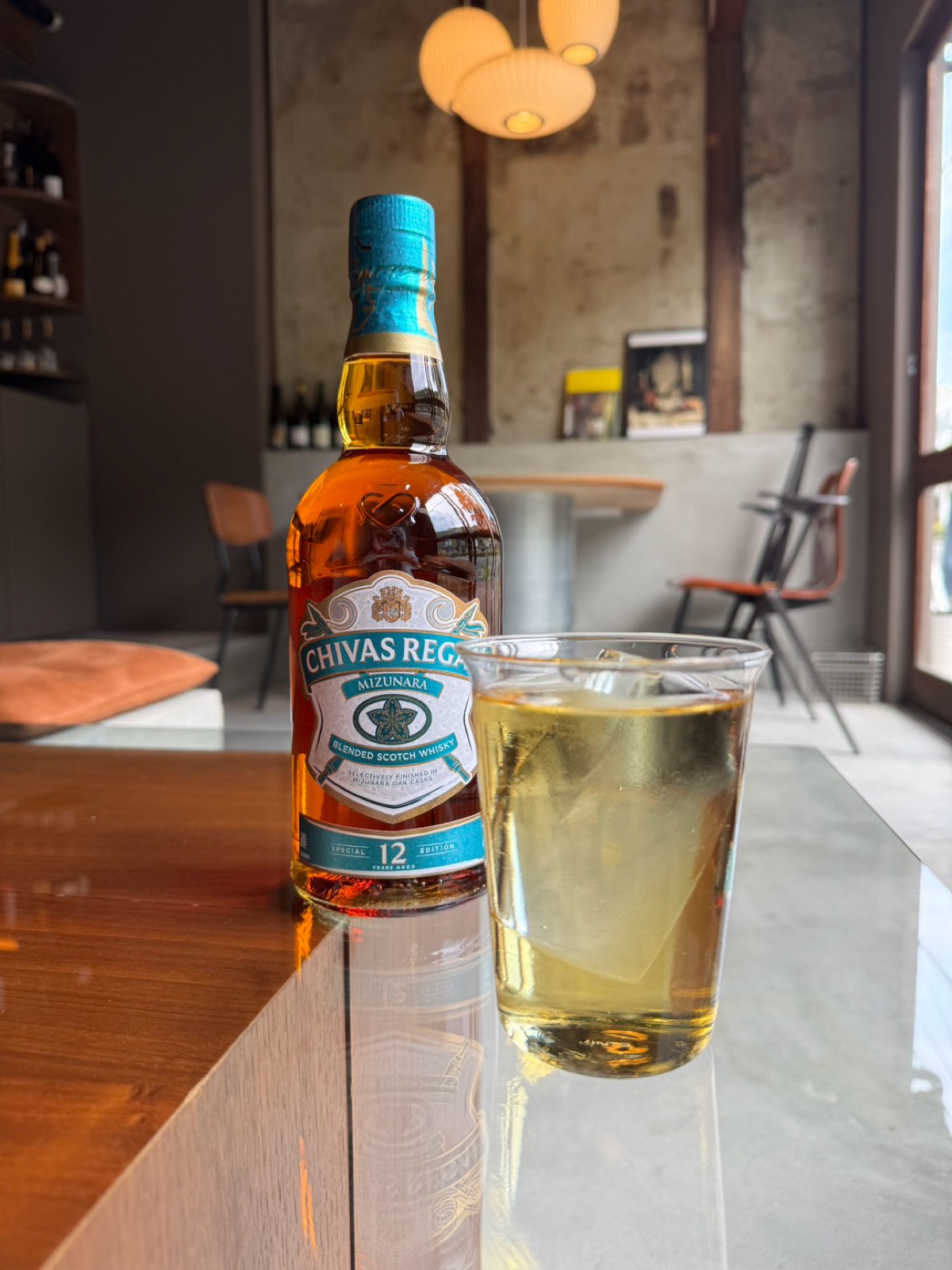 The highball at Bello Vero — a bottle of Chivas Regal Mizunara 12 Year and a pale-gold highball in a rocks glass on a wooden counter, with a Nelson lantern pendant glowing in the background